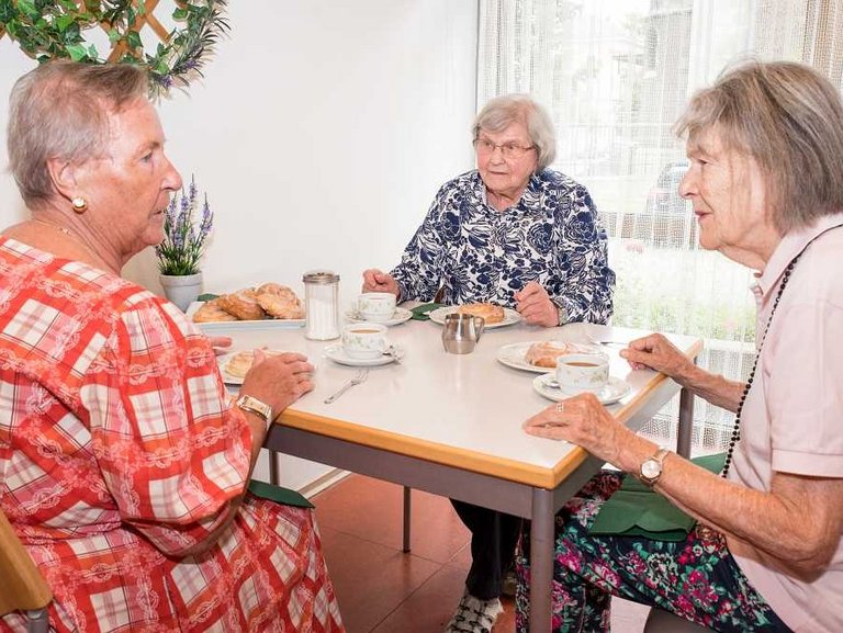 Drei Frauen sitzen am Kaffeetisch, unterhalten sich und essen Gebäck zum Kaffee