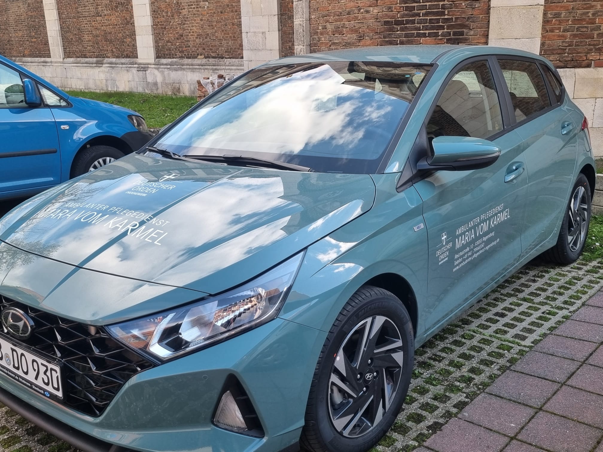 Auto mit der Aufschrift des mobilen Pflegedienstes Regensburg steht vor einer Backsteinhauswand.